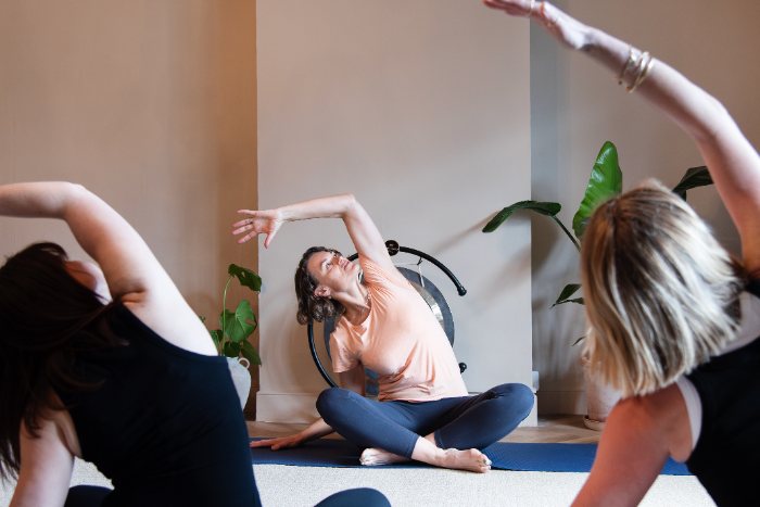 Sarah (teacher), two female clients, seated side stretch - Photographer Emily Dyer